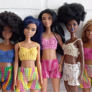 May include: Six dolls wearing crocheted tops and shorts in various colors, including rainbow, yellow, pink, white, and purple.