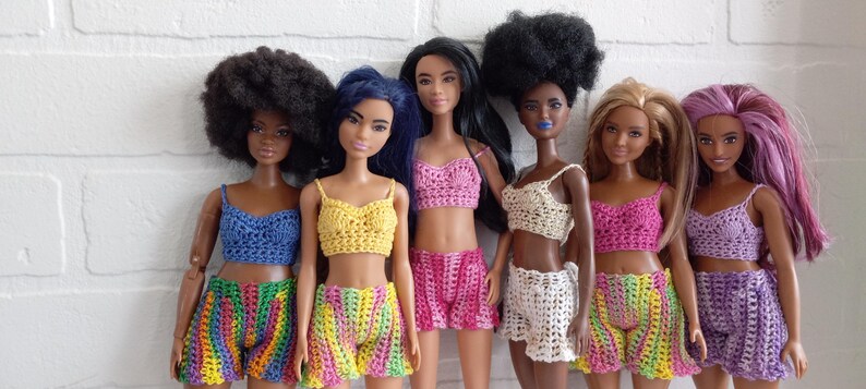 May include: Six dolls wearing crocheted tops and shorts in various colors, including rainbow, yellow, pink, white, and purple.