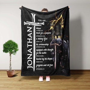 May include: Black fleece blanket with a Christian cross and a lion's face. The text reads "JONATHAN YOU ARE... chosen (1 PETER 2:9) made for a purpose (EPHESIANS 2:10) a child of God (JOHN 1:12) his workmanship (EPHESIANS 2:10) equipped with strength for the battle (PSALM 18:39) healed by his stripes (ISAIAH 53:5) forgiven and set free (EPHESIANS 1:7)"