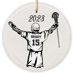 May include: A black and white illustration of a lacrosse player with their arms raised in the air. The player is wearing a jersey with the name "BRADY" and the number "15" on the back. The year "2023" is printed above the player.