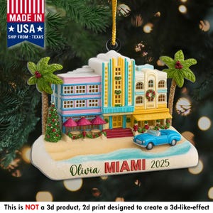 May include: A colorful Christmas ornament featuring a Miami beach scene with buildings, palm trees, and a blue convertible car. The ornament has the text "Olivia MIAMI 2025" and is made in the USA.