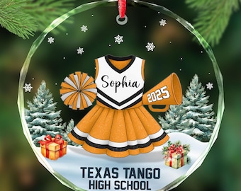 May include: A round, clear glass ornament with a cheerleader design. The ornament features a cheerleader uniform in orange, white, and black, with the name "Sophia" and the year "2025". The text "Texas Tango High School" is at the bottom.