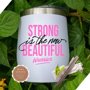 Puede incluir: Un vaso aislado blanco con tapa plateada, con el texto "STRONG is the new BEAUTIFUL Warrior" en rosa y negro. Incluye pajitas de acero inoxidable y una peque&ntilde;a bolsa de transporte. Rodeado de hojas verdes.