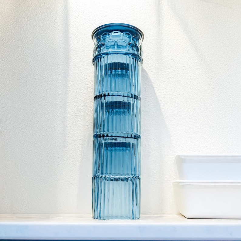 May include: A stackable set of four blue glass containers with a ribbed design. The containers are stacked on top of each other, creating a tall cylinder.