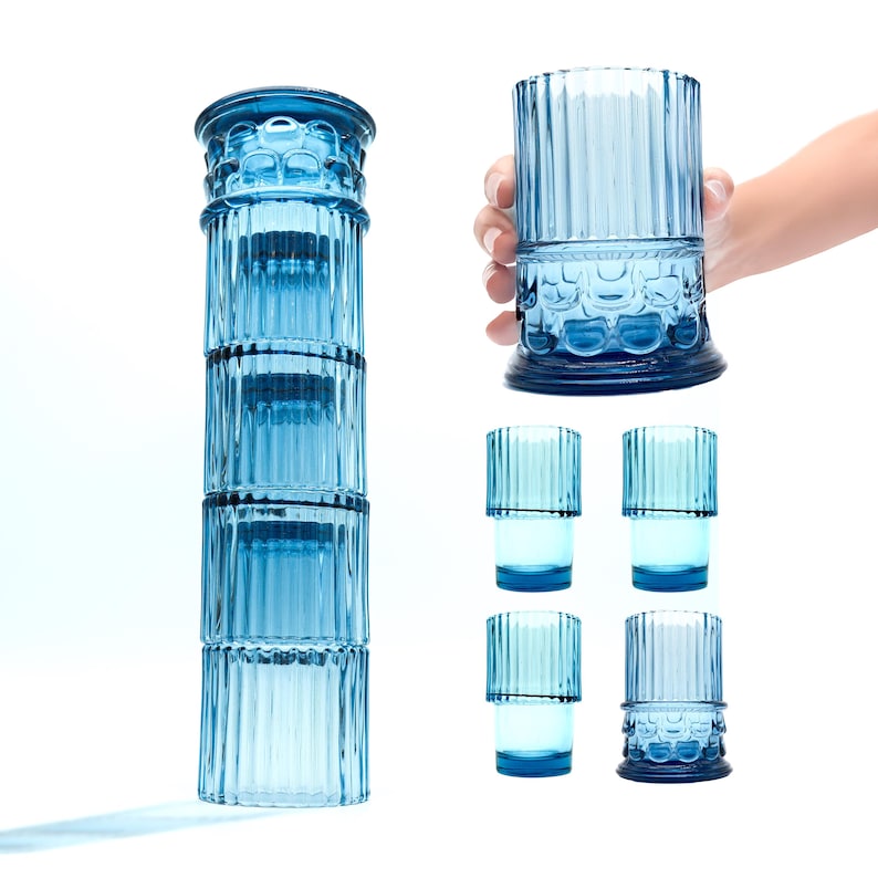 May include: Set of six blue glass tumblers with a fluted design. The tumblers are stacked in a tower, with one tumbler being held in a hand.