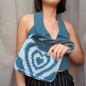 May include: A blue crocheted halter top with a white crocheted bag. The bag has a swirl pattern.