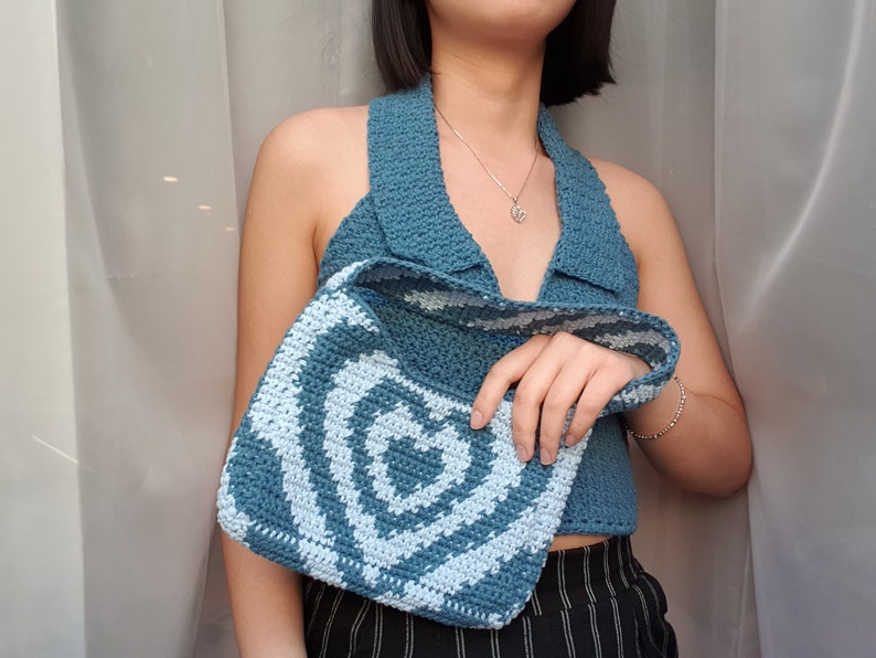 May include: A blue crocheted halter top with a white crocheted bag. The bag has a swirl pattern.