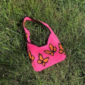 May include: A pink crocheted tote bag with a black trim and orange butterfly designs.