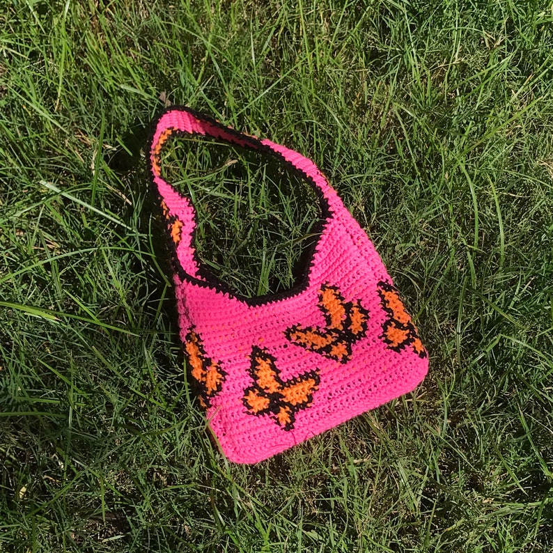 May include: A pink crocheted tote bag with a black trim and orange butterfly designs.