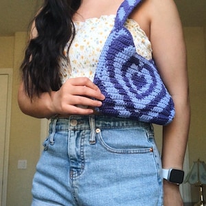 May include: A purple and blue crocheted bag with a circular pattern. The bag has a long strap and is worn over the shoulder.