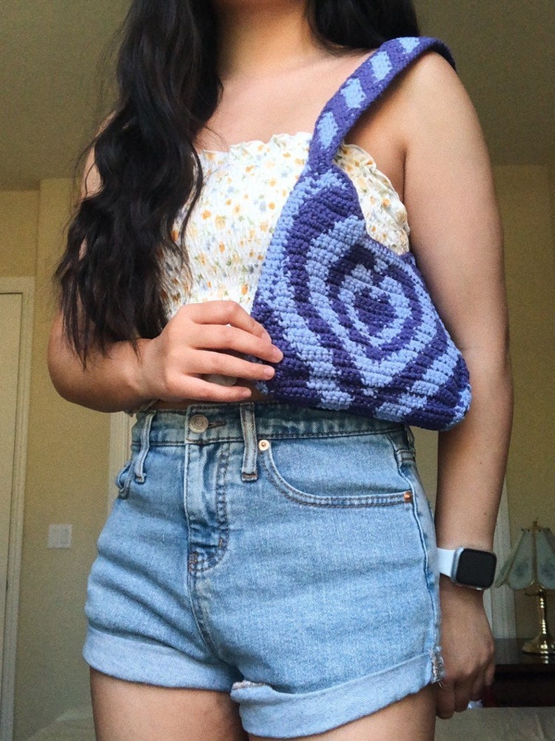 May include: A purple and blue crocheted bag with a circular pattern. The bag has a long strap and is worn over the shoulder.