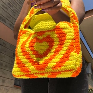 May include: A yellow and orange crocheted tote bag with a heart design.