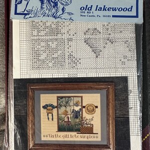 May include: A cross-stitch pattern for a framed embroidery design titled "'tis the gift to be simple". The design features a window with a view of a birdhouse, a bird, and a basket of flowers. The pattern is from "old lakewood" and is priced at $5.95.
