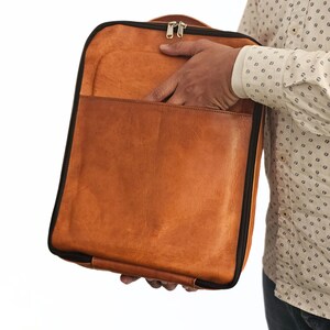 May include: A brown leather laptop bag with a black zipper and black trim. The bag is open and the inside is visible.