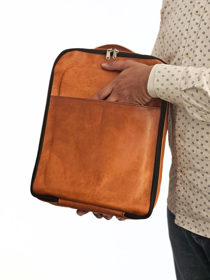 May include: A brown leather laptop bag with a black zipper and black trim. The bag is open and the inside is visible.