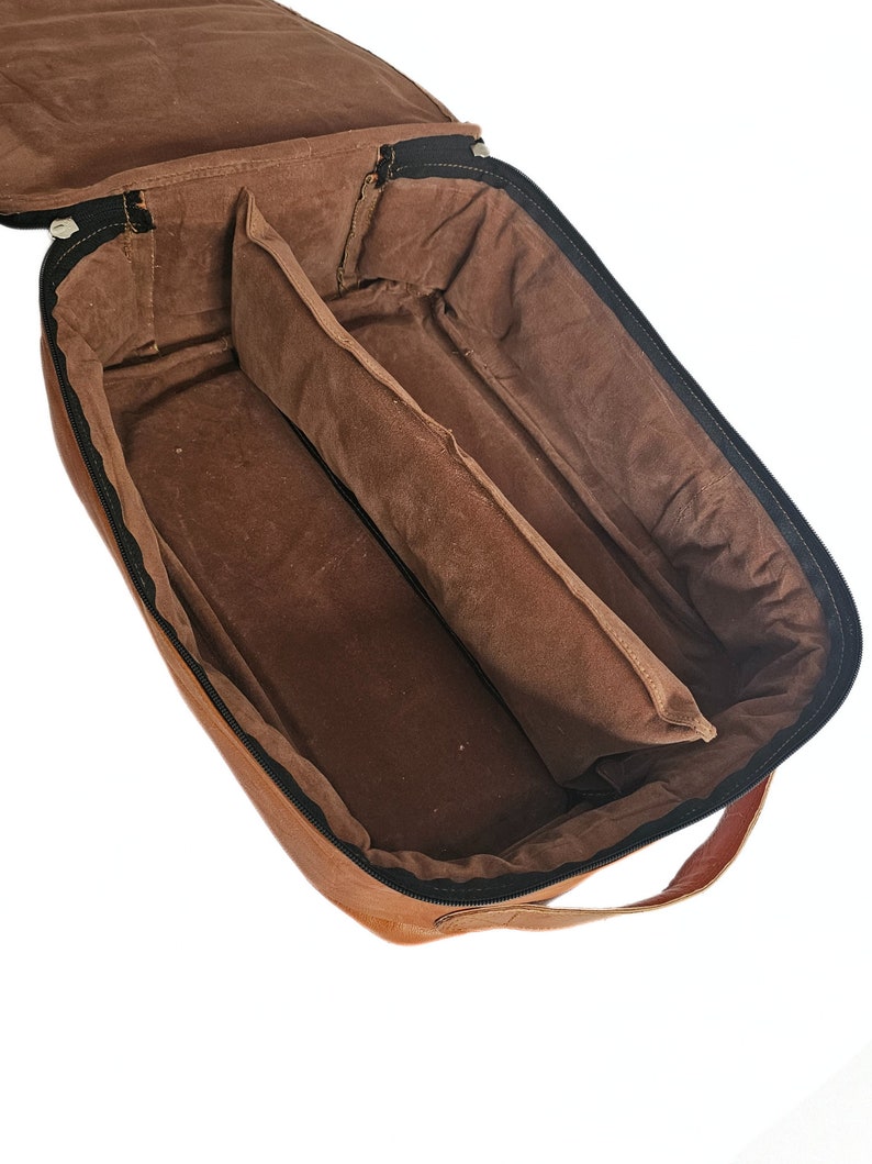 May include: A brown leather travel bag with a zip closure and a handle. The bag is open and the interior is lined with brown fabric. The bag has two compartments.