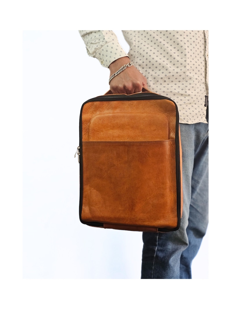 May include: A brown leather backpack with a black zipper and trim. The backpack has a large main compartment and a smaller front pocket.