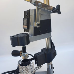 May include: A silver and black metal heat press machine with a digital temperature display and a lever. The machine has a black base and a silver metal arm. The machine is used for pressing heat transfer vinyl onto fabric.