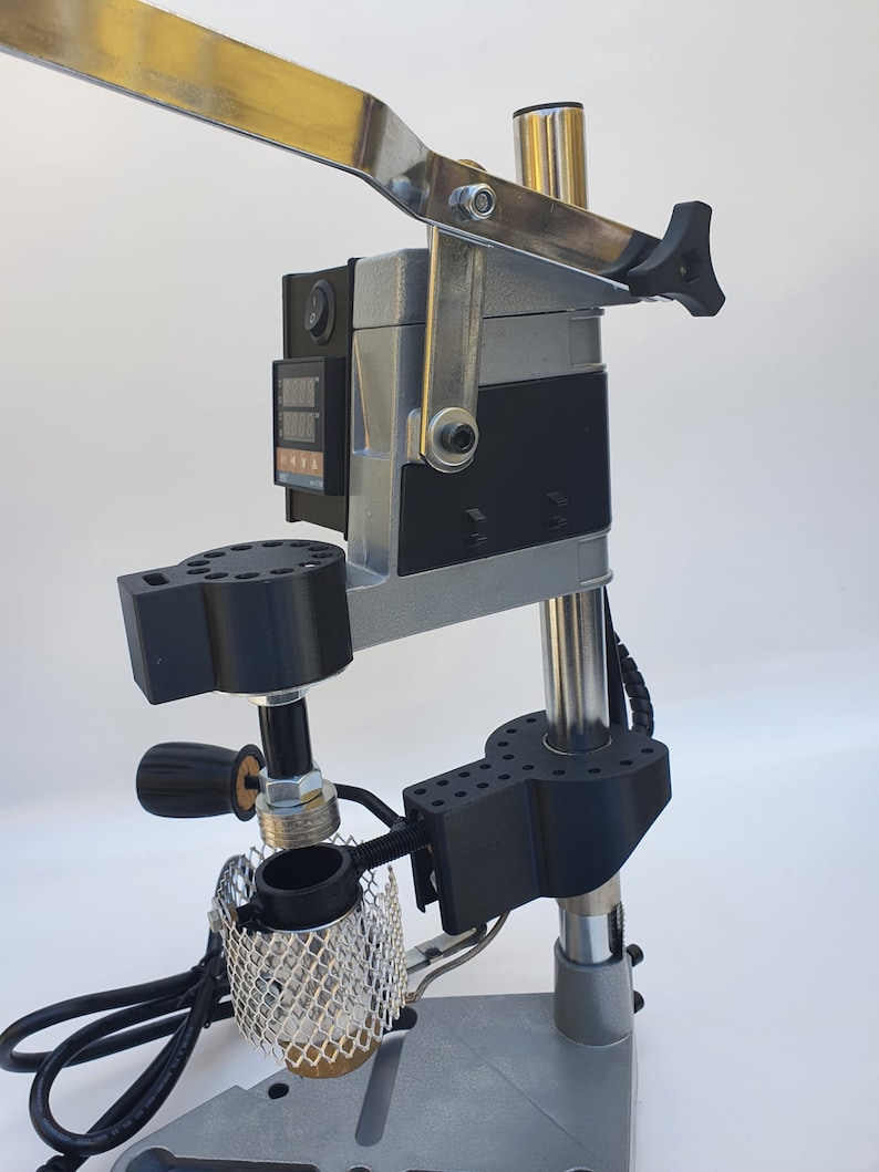 May include: A silver and black metal heat press machine with a digital temperature display and a lever. The machine has a black base and a silver metal arm. The machine is used for pressing heat transfer vinyl onto fabric.