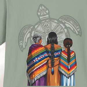 May include: Three women, wearing colorful patterned shawls, stand in front of a stylized turtle design. The women are facing a large, gray turtle with a circular design on its shell. The women are wearing traditional clothing and have long, dark hair.
