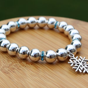 May include: A silver bracelet with a snowflake charm. The bracelet is made of round beads with a row of blue crystals on each side.