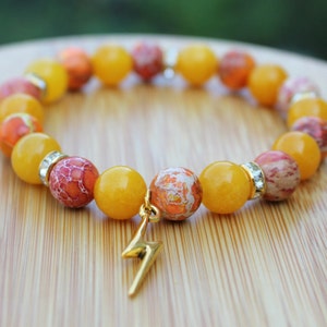 May include: A yellow and orange gemstone bracelet with a gold lightning bolt charm. The bracelet is made of round beads and has a sparkly accent bead.