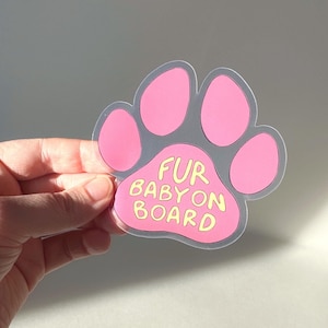 May include: Pink paw print car sticker with the text "Fur Baby On Board" in yellow lettering.