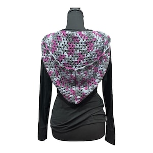 Op de afbeelding: Een handgemaakte gehaakte sjaal in een granny square patroon. De sjaal heeft een kleurenschema van grijs, wit en magenta. De sjaal wordt getoond op een zwarte mannequin, die de driehoekige vorm en de drapeering laat zien.