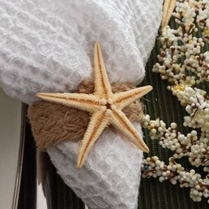 May include: A white cloth napkin with a brown rope tied around it and a starfish on top. The napkin is on a green placemat with white flowers.