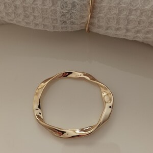 May include: A gold-colored metal napkin ring with a twisted, irregular shape.
