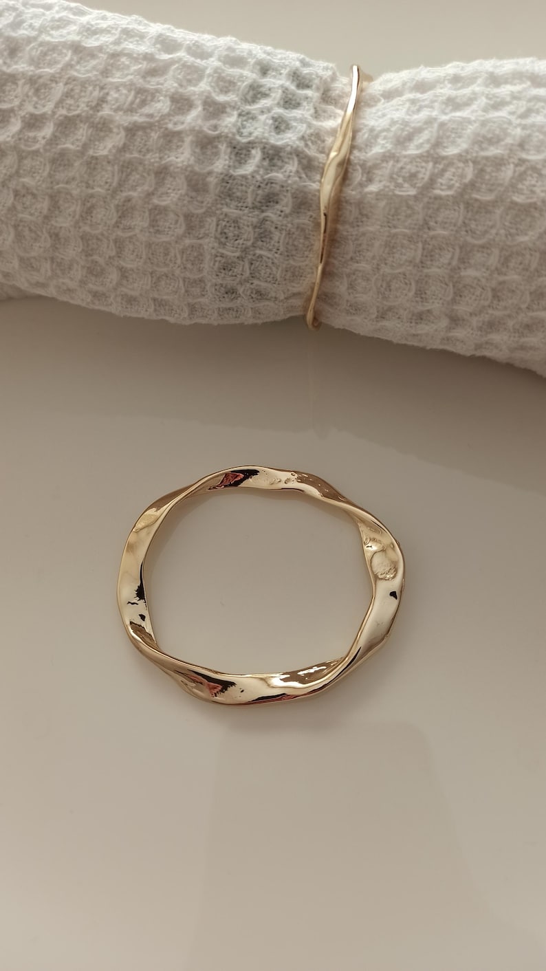May include: A gold-colored metal napkin ring with a twisted, irregular shape.