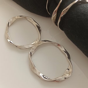 May include: Two silver napkin rings with a wavy, organic design. The rings are made of metal and have a polished finish.