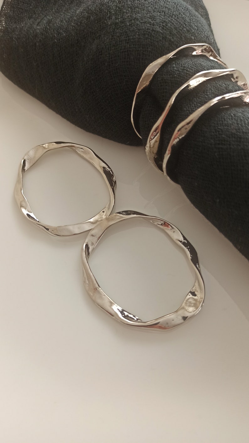 May include: Two silver napkin rings with a wavy, organic design. The rings are made of metal and have a polished finish.