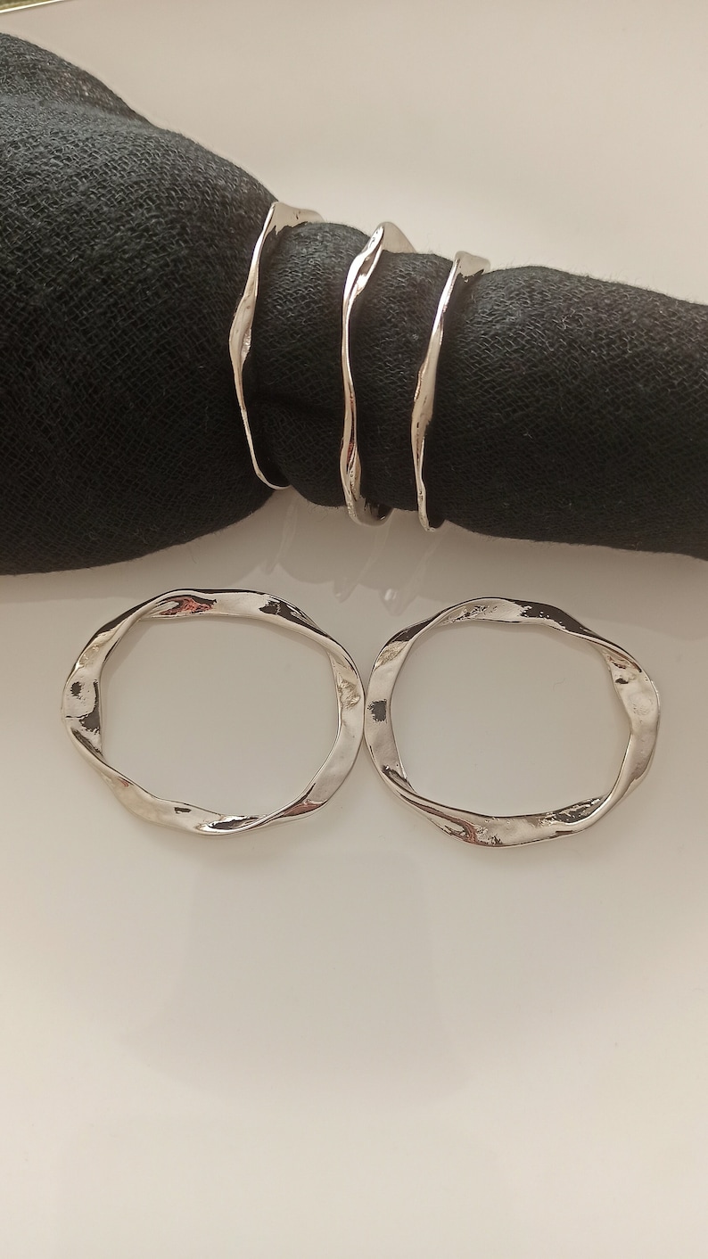 May include: Two silver napkin rings with a wavy, organic design. The rings are made of metal and have a polished finish.