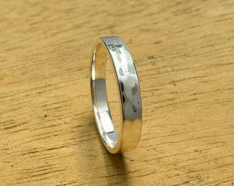 Könnte beinhalten: Ein silberner Ring mit gehammerter Textur. Der Ring ist auf einer Holzoberfläche platziert. Der Ring hat eine polierte Oberfläche und ein schlichtes, elegantes Design. Der Schmuck stammt von GSNJEWELS.