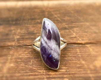 May include: A silver ring with a large, purple and white amethyst stone. The stone is set in a simple, curved band.