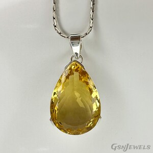 May include: A silver necklace with a large, pear-shaped yellow gemstone pendant. The pendant is a vibrant yellow color and is suspended from a silver chain. The gemstone is faceted, catching the light.