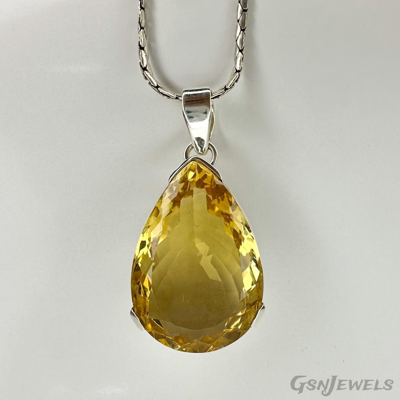 May include: A silver necklace with a large, pear-shaped yellow gemstone pendant. The pendant is a vibrant yellow color and is suspended from a silver chain. The gemstone is faceted, catching the light.