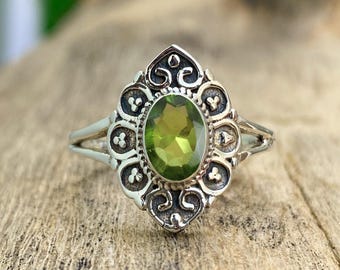 May include: A silver ring with an oval green gemstone set in a detailed filigree design.