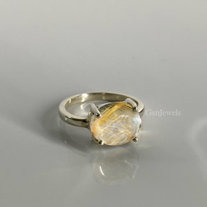 May include: A silver ring featuring a large oval-shaped golden rutilated quartz gemstone. The gemstone has a clear, glassy appearance with golden inclusions.