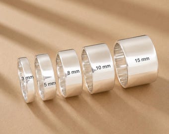 Könnte beinhalten: Ein Set aus fünf polierten, silberfarbenen Ringen, die in einer Reihe angeordnet sind und von links nach rechts an Breite zunehmen. Die Ringe sind mit ihren Breiten von 3 mm, 5 mm, 8 mm, 10 mm und 15 mm beschriftet und schlicht gestaltet.