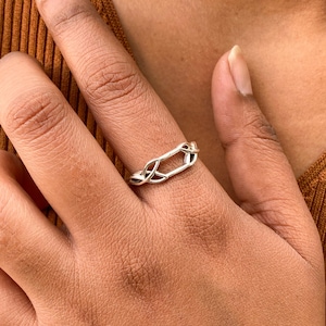 Puede incluir: Un anillo de plata con un diseño tejido. El anillo está hecho de una sola pieza de metal que se tuerce y entrelaza para crear un patrón único e intrincado.
