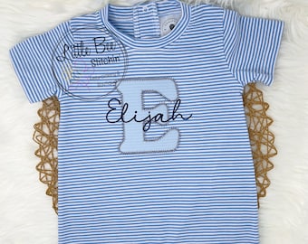 May include: A blue and white striped baby onesie with a large blue felt letter E and the name Elijah embroidered in black thread.
