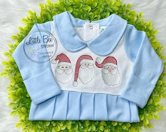 May include: A light blue baby onesie with a white panel featuring three embroidered Santa faces. The onesie has a Peter Pan collar and long sleeves. The text "Little Bee Stichin' Embroidery & Boutique" is visible in the top left corner.