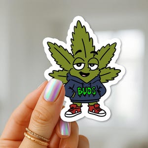 Puede incluir: Una pegatina de vinilo troquelada que muestra un personaje de hoja de cannabis de dibujos animados con expresión somnolienta, vistiendo una sudadera azul oscuro con la palabra BUDS en verde y zapatillas rojas con cordones y suelas blancas.
