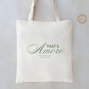 May include: A white canvas tote bag with green text that reads "That's Amore" with the names Gavin and Emily and the location Sicily 2024 printed below.