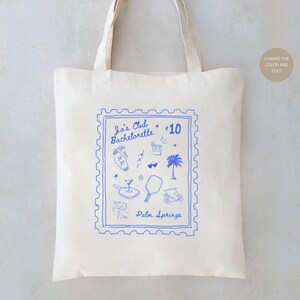 May include: A white tote bag with a blue stamp design featuring the text "Jo's Club Bachelorette * 10 Palm Springs". The stamp includes various illustrations of palm trees, cocktails, sunglasses, and other vacation-themed items.