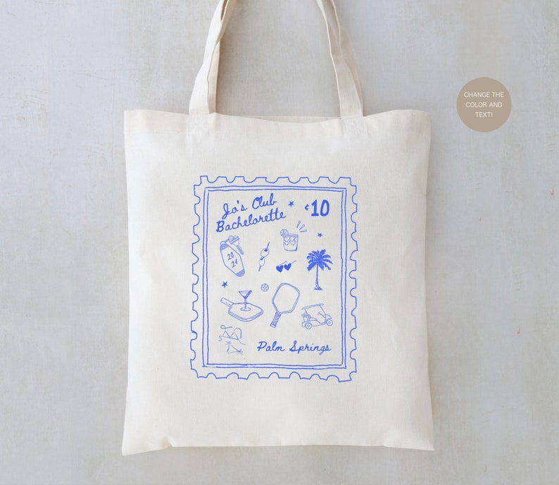 May include: A white tote bag with a blue stamp design featuring the text "Jo's Club Bachelorette * 10 Palm Springs". The stamp includes various illustrations of palm trees, cocktails, sunglasses, and other vacation-themed items.