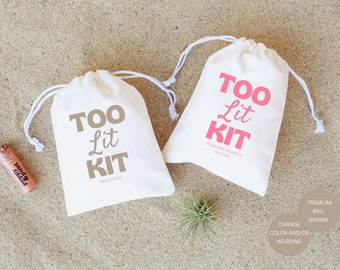 May include: Two white drawstring bags with the text "Too Lit Kit" printed on them in pink and brown. The bag on the left has the text "Mexico 2014" printed below the main text. The bag on the right has the text "Tatums Bachelorette July 2014" printed below the main text.