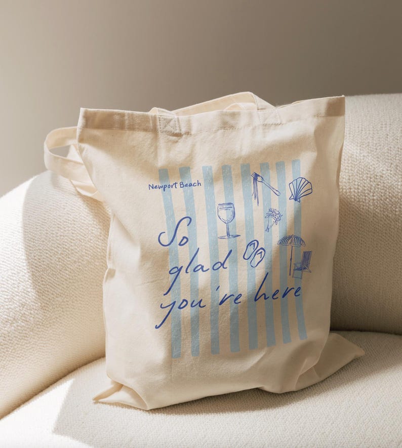 May include: Off-white canvas tote bag with blue vertical stripes and beach-themed illustrations. Text reads "Newport Beach" and "So glad you're here" in blue script. Features a wine glass, flip-flops, and a seashell.